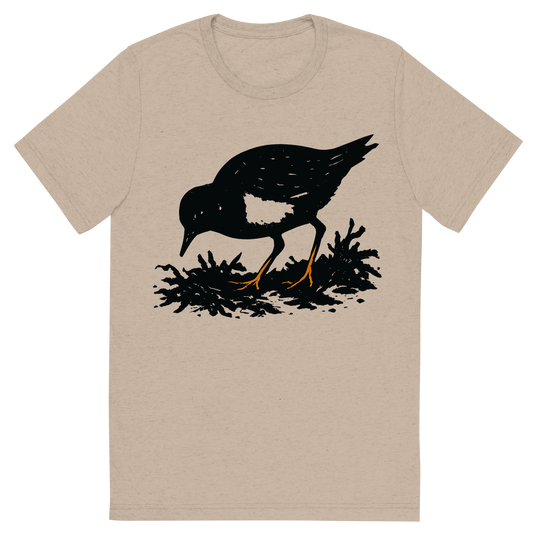 Front view of a Premium Tri-Blend Crew Neck T-Shirt in Tan showing 'A high-contrast silhouette with minimal accent color, busy graphic of a small, blocky silhouette of a ruddy turnstone foraging near seaweed, orange legs and white chest accent, transparent background, optimized for dtg printing'