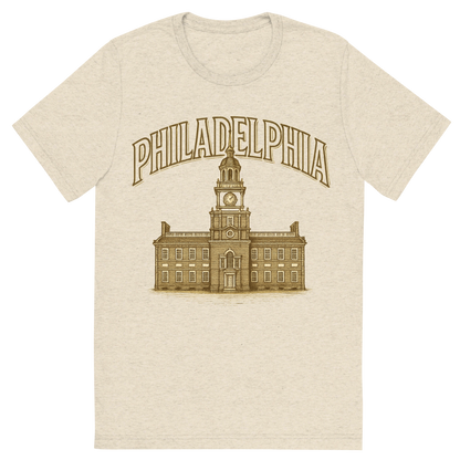 Front view of a Premium Tri-Blend Crew Neck T-Shirt in Oatmeal showing 'A typographic, nostalgic graphic of a typographic illustration of the words 'philadelphia' with a vintage line art drawing of independence hall'