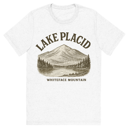 Front view of a Premium Tri-Blend Crew Neck T-Shirt in Solid White showing 'A typographic, nostalgic graphic of a typographic illustration of the words 'lake placid' with a vintage line art drawing of whiteface mountain'