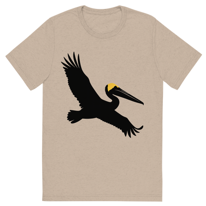 Front view of a Premium Tri-Blend Crew Neck T-Shirt in Tan showing 'A high-contrast silhouette with minimal accent color, majestic graphic of a large silhouette of a brown pelican gliding with wings stretched and pouch visible, yellow crown highlighted in color, transparent background, optimized for dtg printing'
