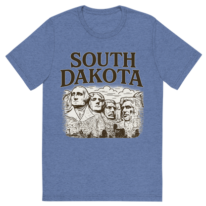 Front view of a Premium Tri-Blend Crew Neck T-Shirt in Blue showing 'A typographic, nostalgic graphic of a typographic illustration of the words 'south dakota' with a vintage line art drawing of the presidential sculptures'