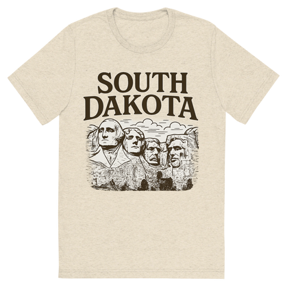 Front view of a Premium Tri-Blend Crew Neck T-Shirt in Oatmeal showing 'A typographic, nostalgic graphic of a typographic illustration of the words 'south dakota' with a vintage line art drawing of the presidential sculptures'